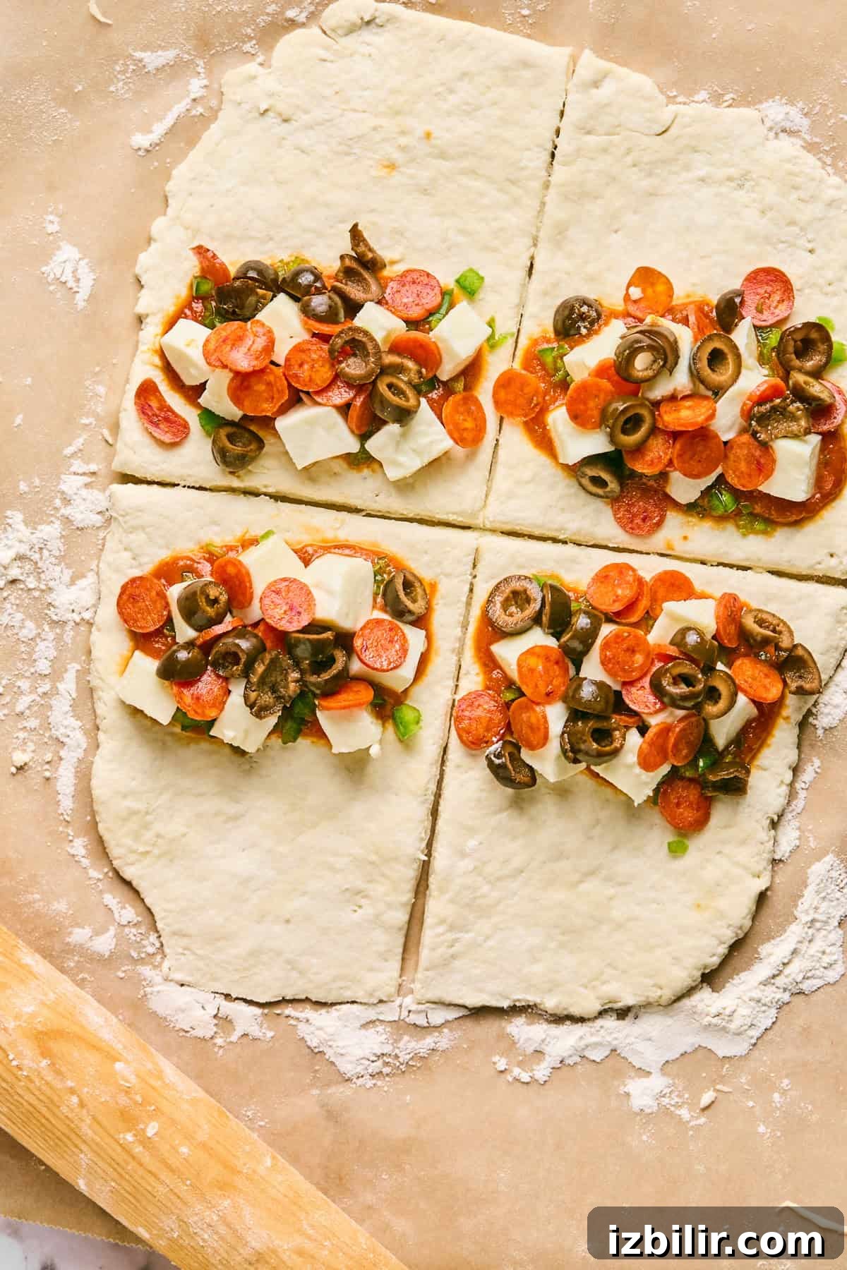 Homemade Protein-Packed Pizza Hot Pockets 3 Four sections of raw dough, resembling pizza hot pockets, are topped with cheese cubes, pepperoni slices, olives, and green onions on a floured surface.