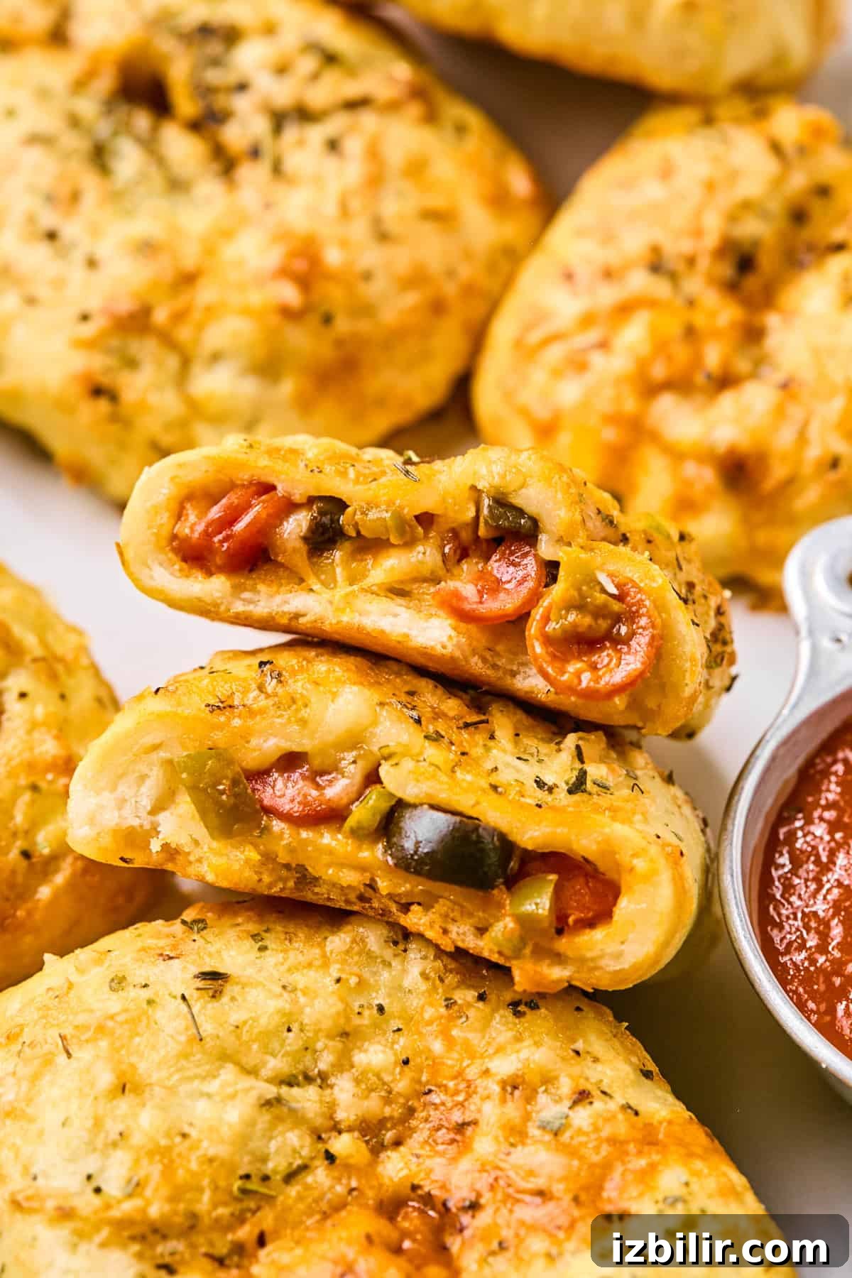 Homemade Protein-Packed Pizza Hot Pockets 4 Close-up of baked calzones, reminiscent of pizza hot pockets, filled with cheese, pepperoni, and vegetables, accompanied by a small dish of marinara sauce.