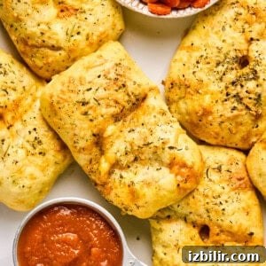 Homemade Protein-Packed Pizza Hot Pockets 5 Golden-brown stuffed bread rolls, reminiscent of delightful pizza hot pockets, are sprinkled with herbs and paired with a small bowl of tomato sauce on a white surface.