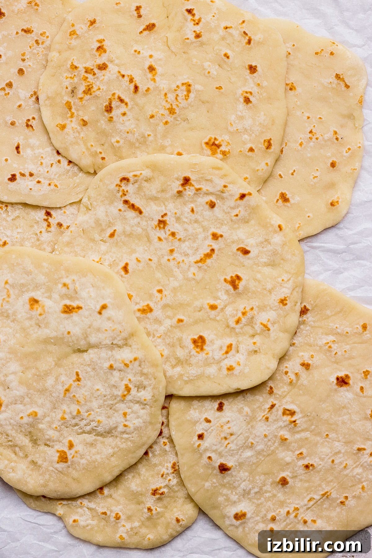 Several pieces of flatbread, slightly browned and overlapping, are laid out on a crumpled white surface.