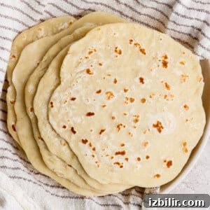 A stack of homemade flour tortillas rests on a striped kitchen towel.