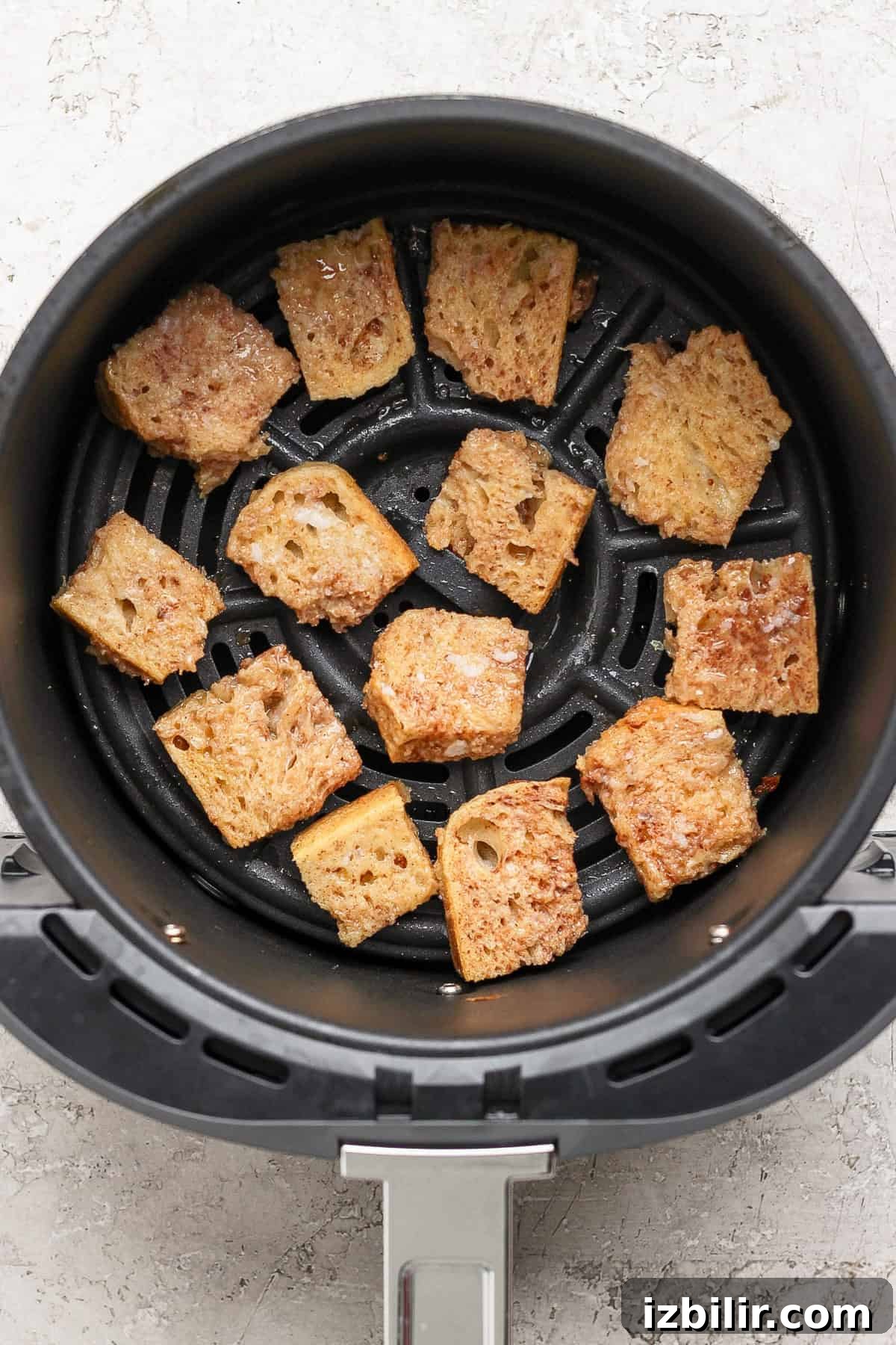 Pieces of bread being toasted in an air fryer basket.