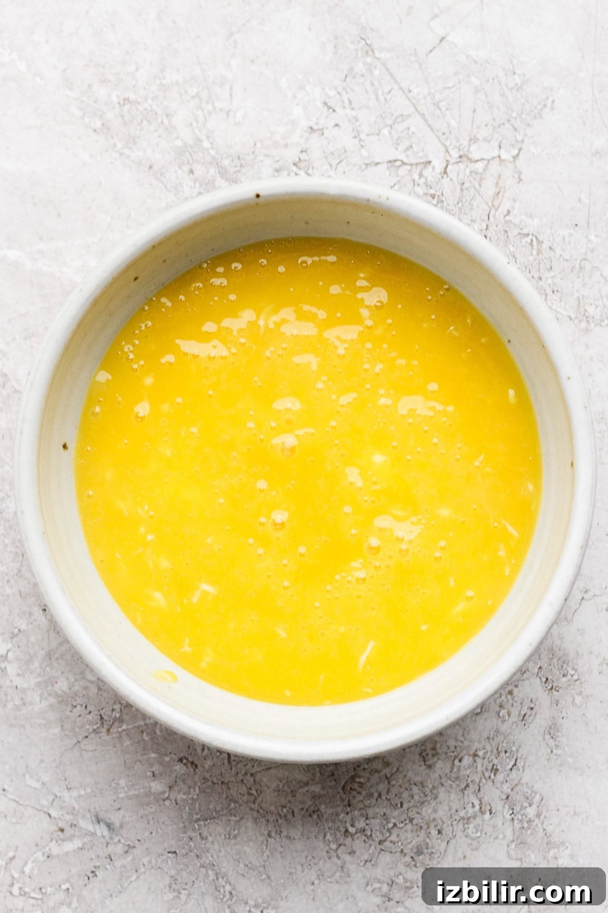 Silky Homemade Honey Lemon Curd for Toasts and Desserts 4 A white bowl filled with beaten eggs on a textured white surface.