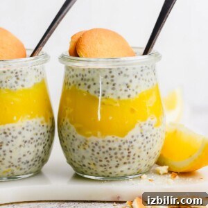 Silky Homemade Honey Lemon Curd for Toasts and Desserts 5 A glass jar layered with chia pudding and yellow lemon curd, topped with a round cookie and a spoon, with a lemon wedge next to the jar.