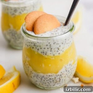 Glass jar filled with chia seed pudding and lemon layer, topped with two cookies and a spoon. Lemon slices are in the background.