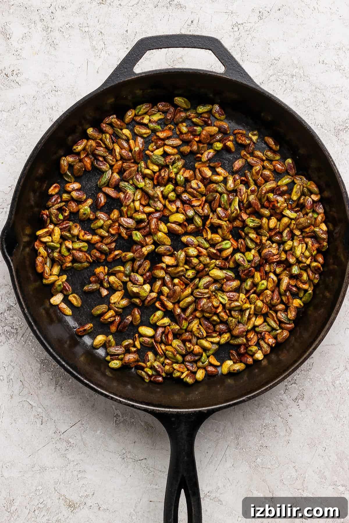 Crisp Summer Salad with Honey-Roasted Pistachios 3 A black cast iron skillet filled with roasted pistachios sits on a light textured surface.