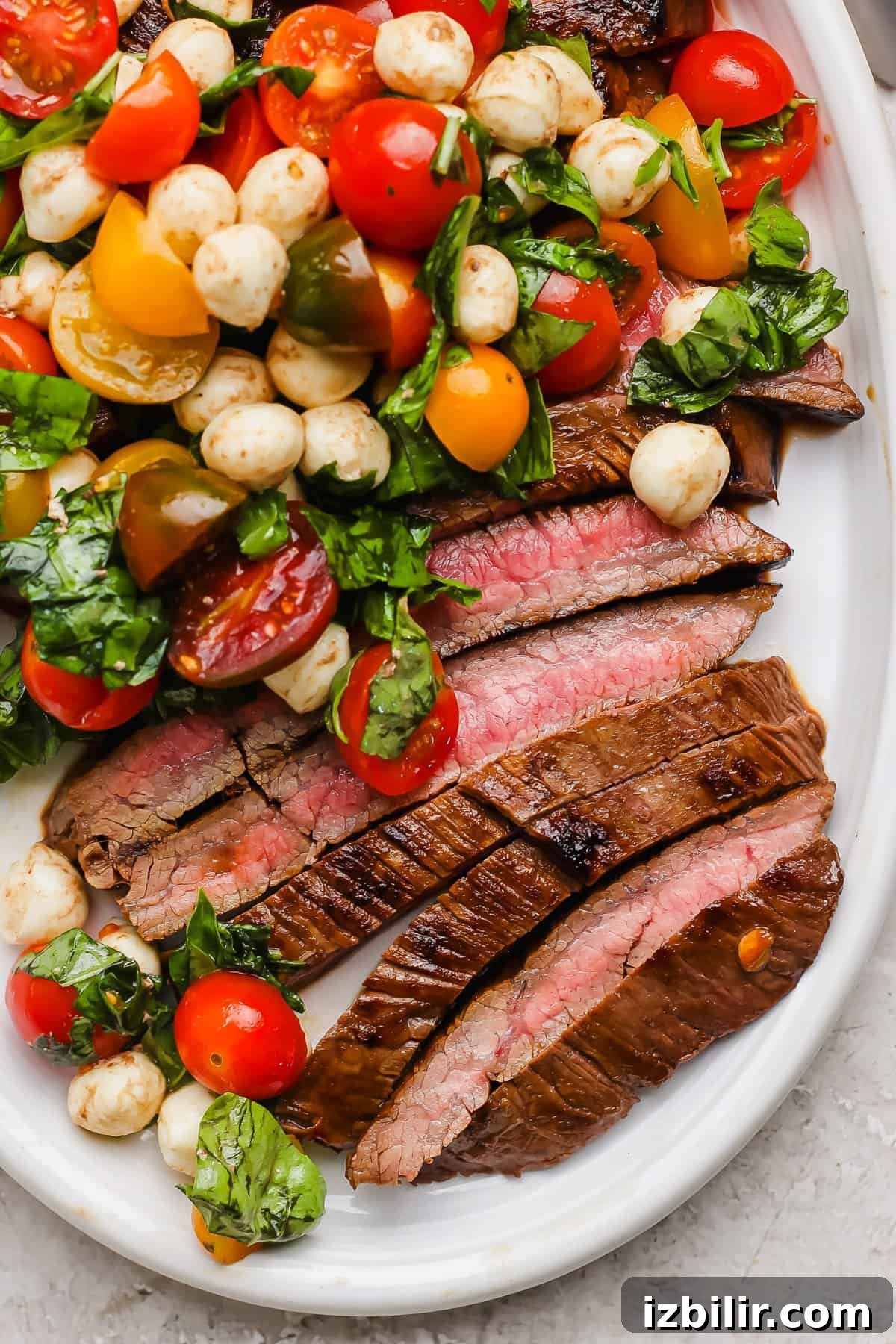Seared Balsamic Steak Caprese with Fresh Mozzarella 2 Sliced medium-rare steak served with a salad of cherry tomatoes, mozzarella balls, and fresh basil on a white plate.