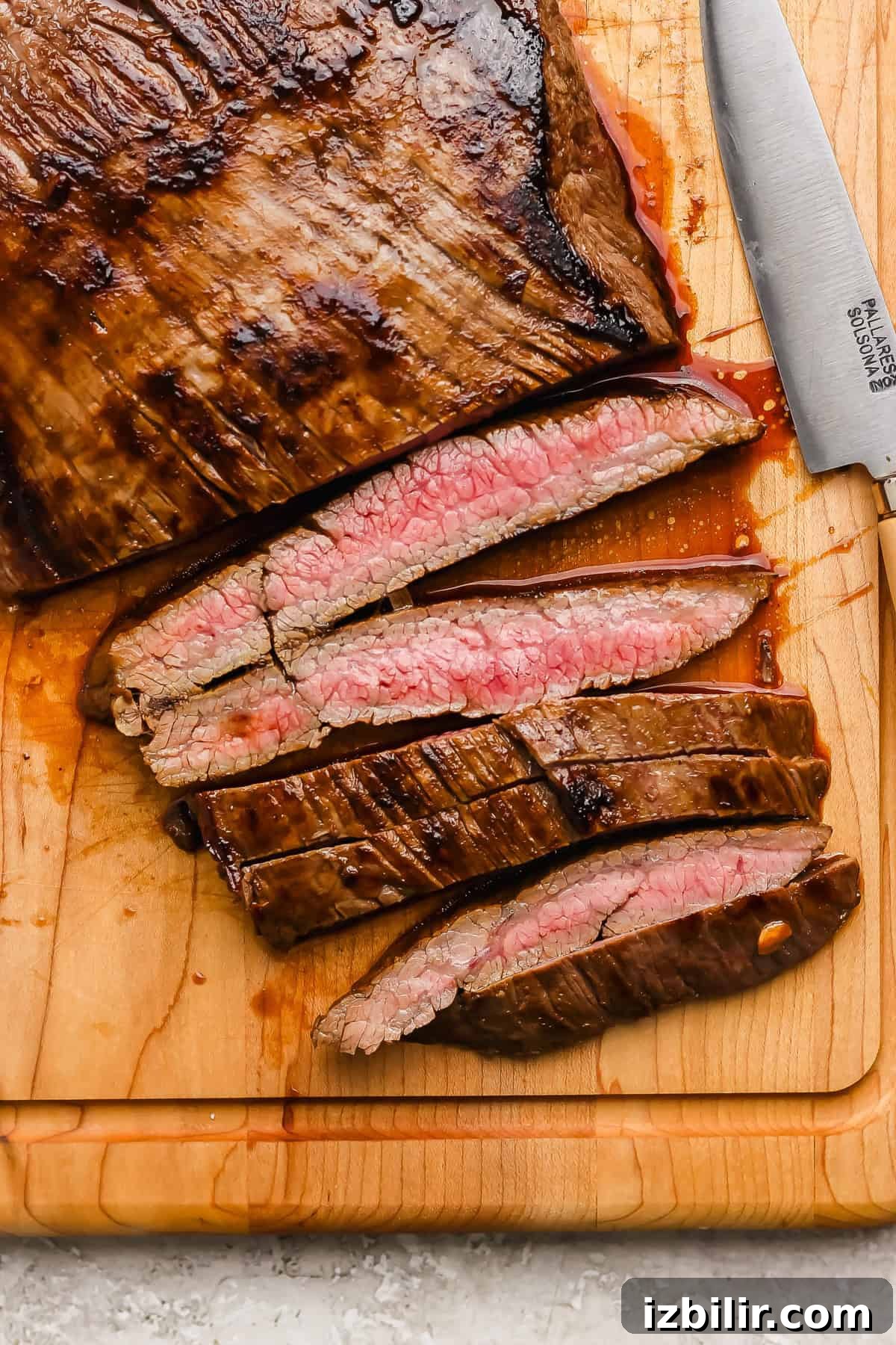 Seared Balsamic Steak Caprese with Fresh Mozzarella 4 Sliced medium-rare steak on a wooden cutting board with a knife beside it.