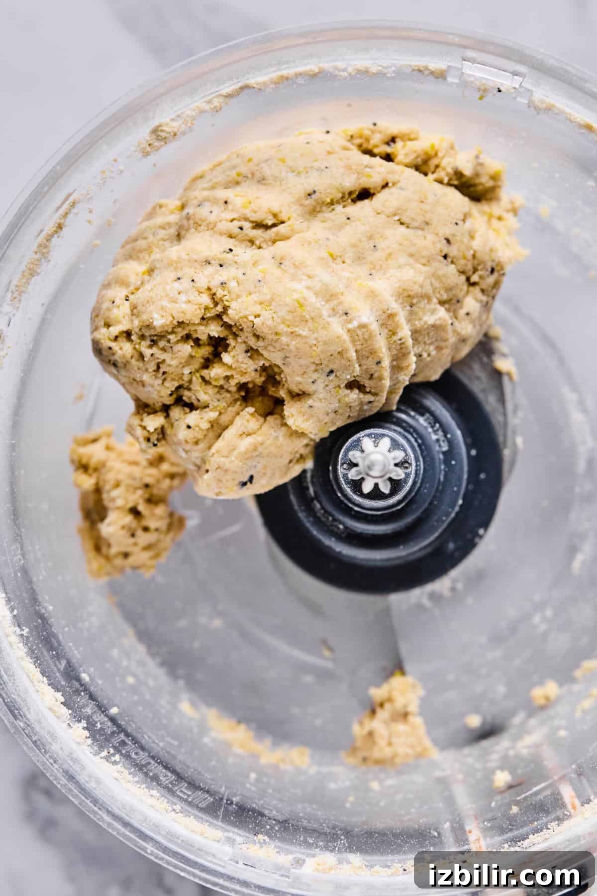 A close-up view of dough formed into a ball inside a food processor with a visible metal blade.
