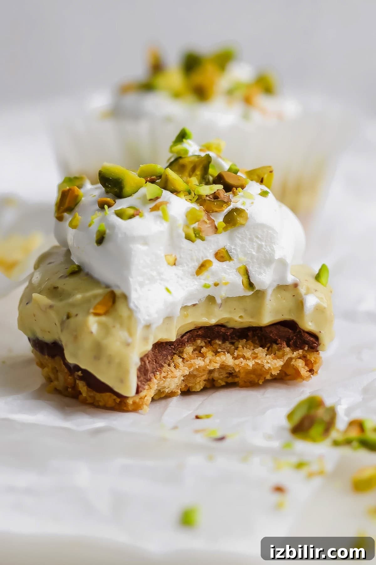 A close-up of a dessert with a crumbly base, creamy middle layer, whipped topping, and chopped pistachios, with a bite taken out of it.