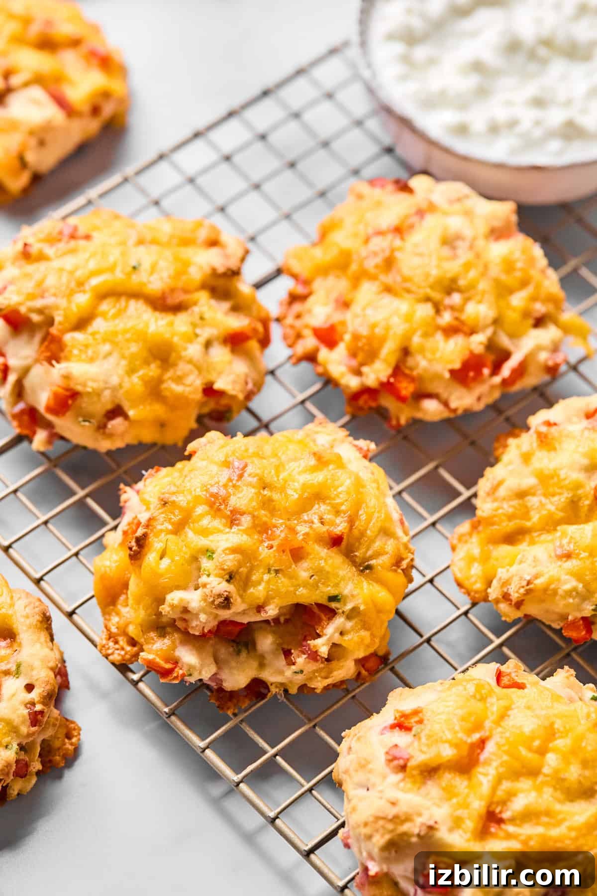 Cheddar and red pepper scones cooling on a wire rack, with a bowl of cottage cheese in the background.