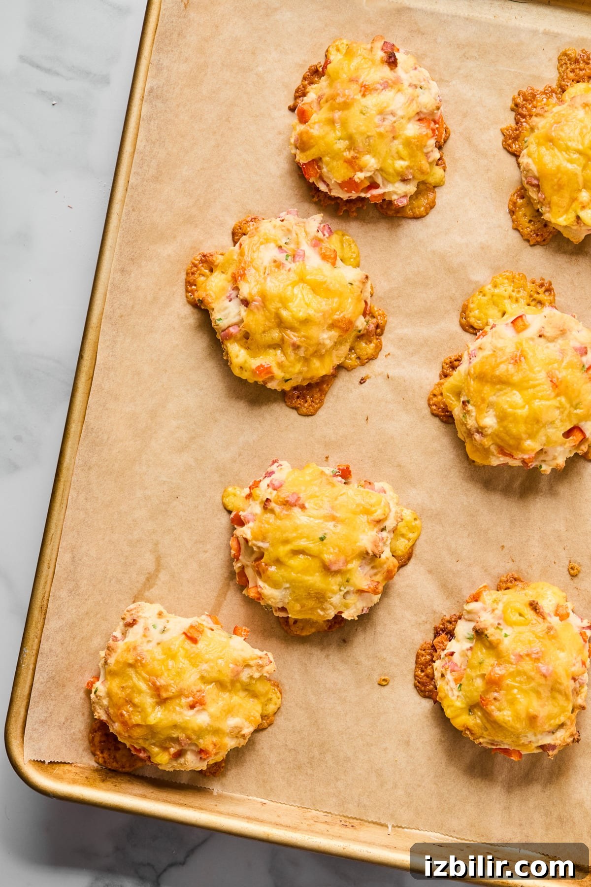 A baking sheet lined with parchment paper holds seven baked savory cheese and vegetable biscuits.