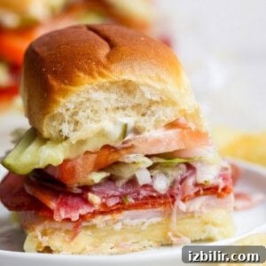 Italian Grinder Sliders Recipe: Classic Mini Italian Sandwiches 5 A small sandwich with sliced meats, cheese, tomato, lettuce, pickles, and mayonnaise on a soft bun, shown with a bite taken out of it.