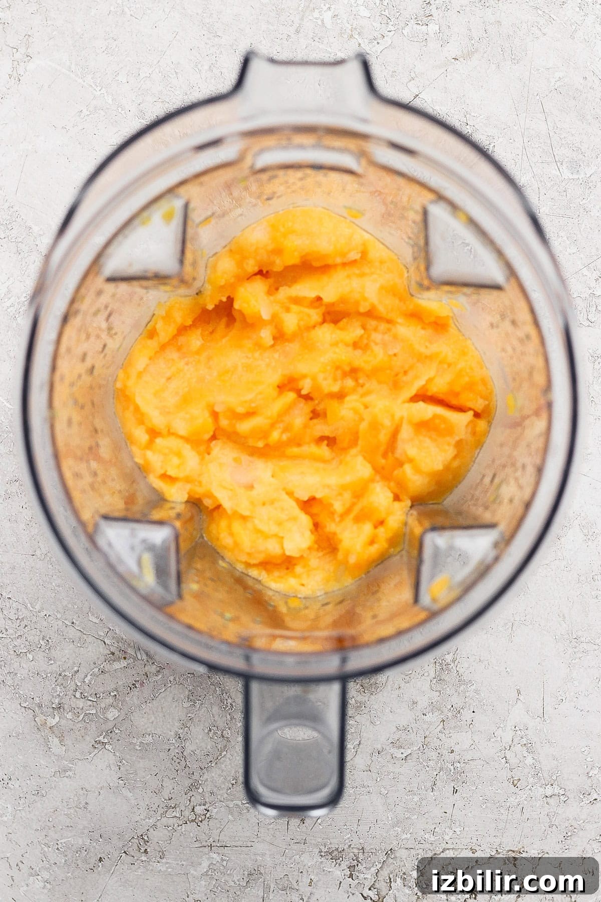 Frozen Peach Bellini: Sparkling Summer Cocktail 4 Top-down view of an open blender containing a smooth, orange-yellow mixture on a light textured surface.