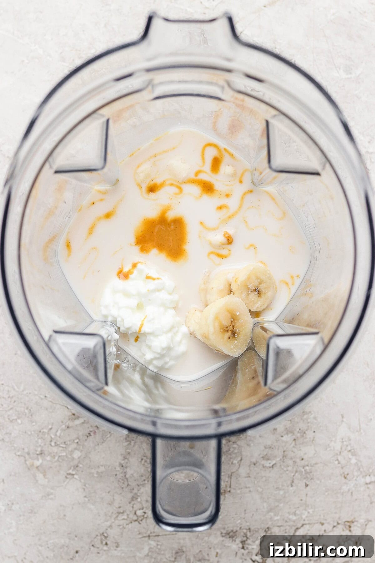 A blender containing milk, sliced banana, cottage cheese, and a drizzle of honey, viewed from above.
