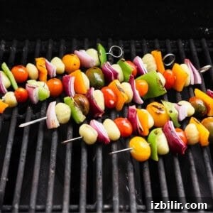 Rainbow Grilled Gnocchi Skewers with Roasted Veggies 7 Vegetable skewers with tomatoes, onions, bell peppers, and gnocchi are grilling on a barbecue grate.