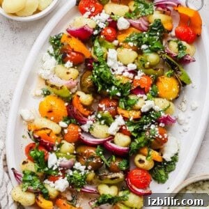Rainbow Grilled Gnocchi Skewers with Roasted Veggies 9 A white platter with vegetable and gnocchi skewers, topped with chopped herbs and crumbled cheese, is pictured next to small bowls of cooked gnocchi and crumbled cheese.