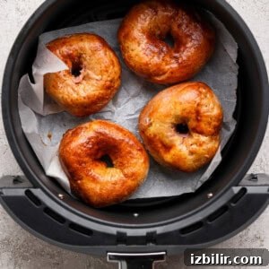 Four golden brown bagels on parchment paper inside an air fryer basket.