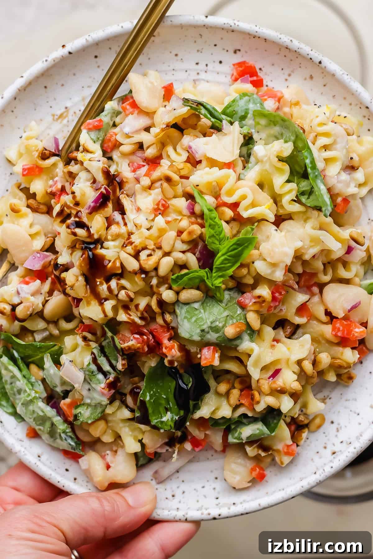 Creamy Cottage Cheese Pasta Salad Recipe 4 A plate of pasta salad with spinach, cannellini beans, red onion, diced red peppers, pine nuts, and a balsamic glaze, served with a fork.