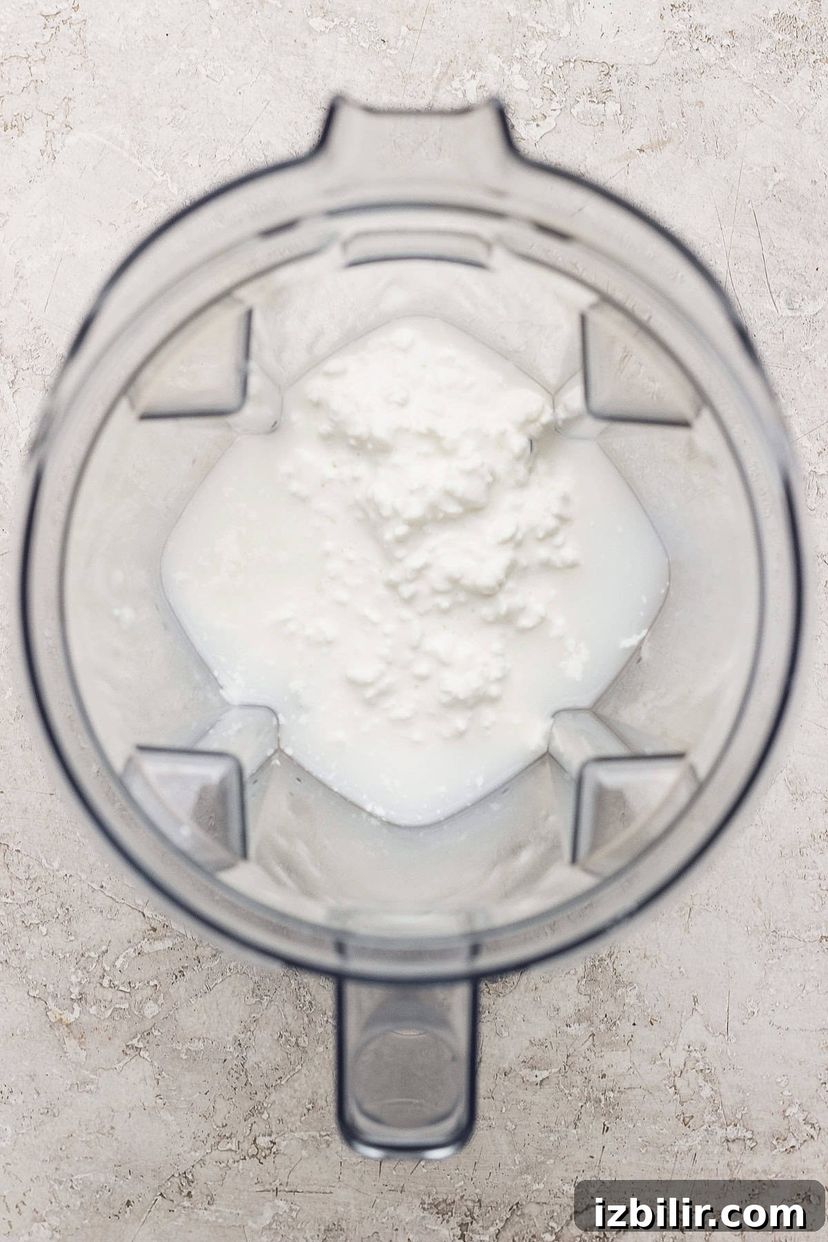 Blender jug with foamy white liquid inside, viewed from above.