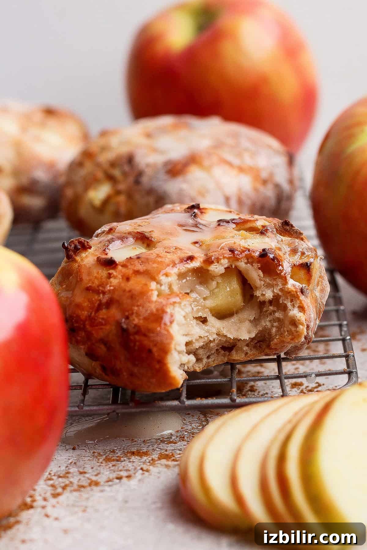 Crispy Air Fryer Apple Fritters with Glaze 2 A partially eaten apple scone sits on a cooling rack, surrounded by whole apples and apple slices.