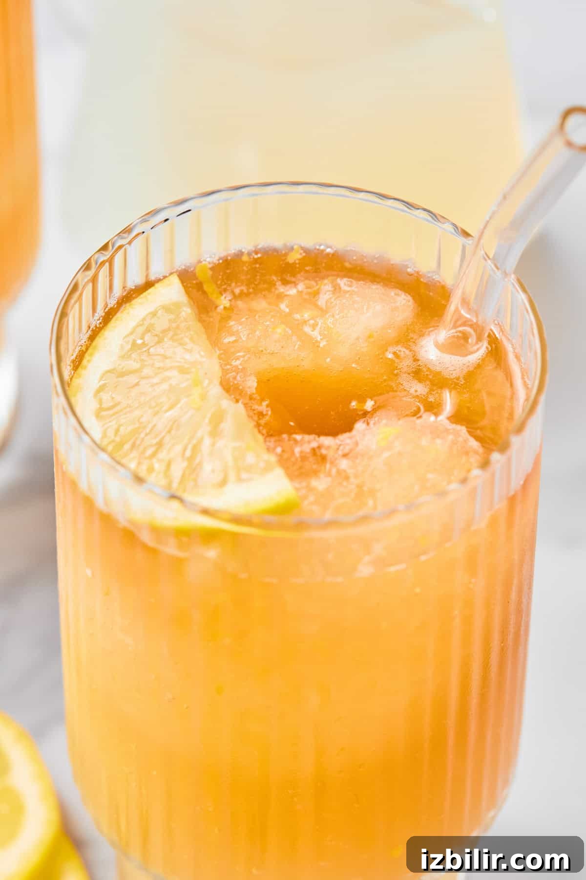 A close-up of an iced orange drink in a ribbed glass with a clear straw and a lemon slice garnish.
