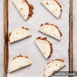 Sheet Pan Tacos with Creamy Avocado Crema Recipe 8 Six folded flour tortillas filled with ground beef are arranged on a parchment-lined baking sheet.