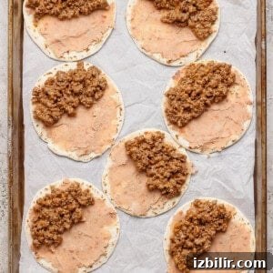 Sheet Pan Tacos with Creamy Avocado Crema Recipe 7 Seven tortillas spread with refried beans and ground beef mixture are arranged on a parchment-lined baking sheet.
