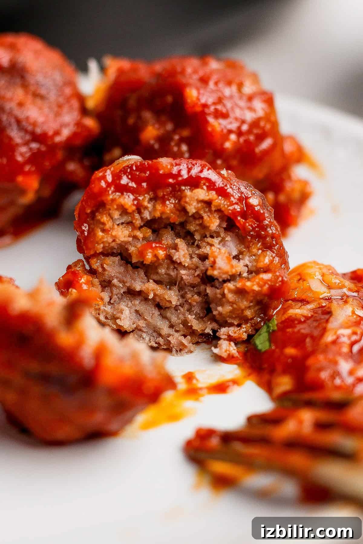 Close-up of meatballs covered in tomato sauce, with one meatball cut open to show the inside texture, on a white plate.