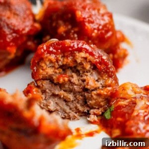 A close-up of a partially eaten meatball covered in tomato sauce, revealing its cooked, ground meat interior.