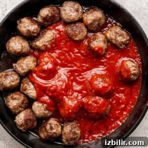 A cast iron skillet filled with meatballs arranged around a pool of tomato sauce on a light textured surface.