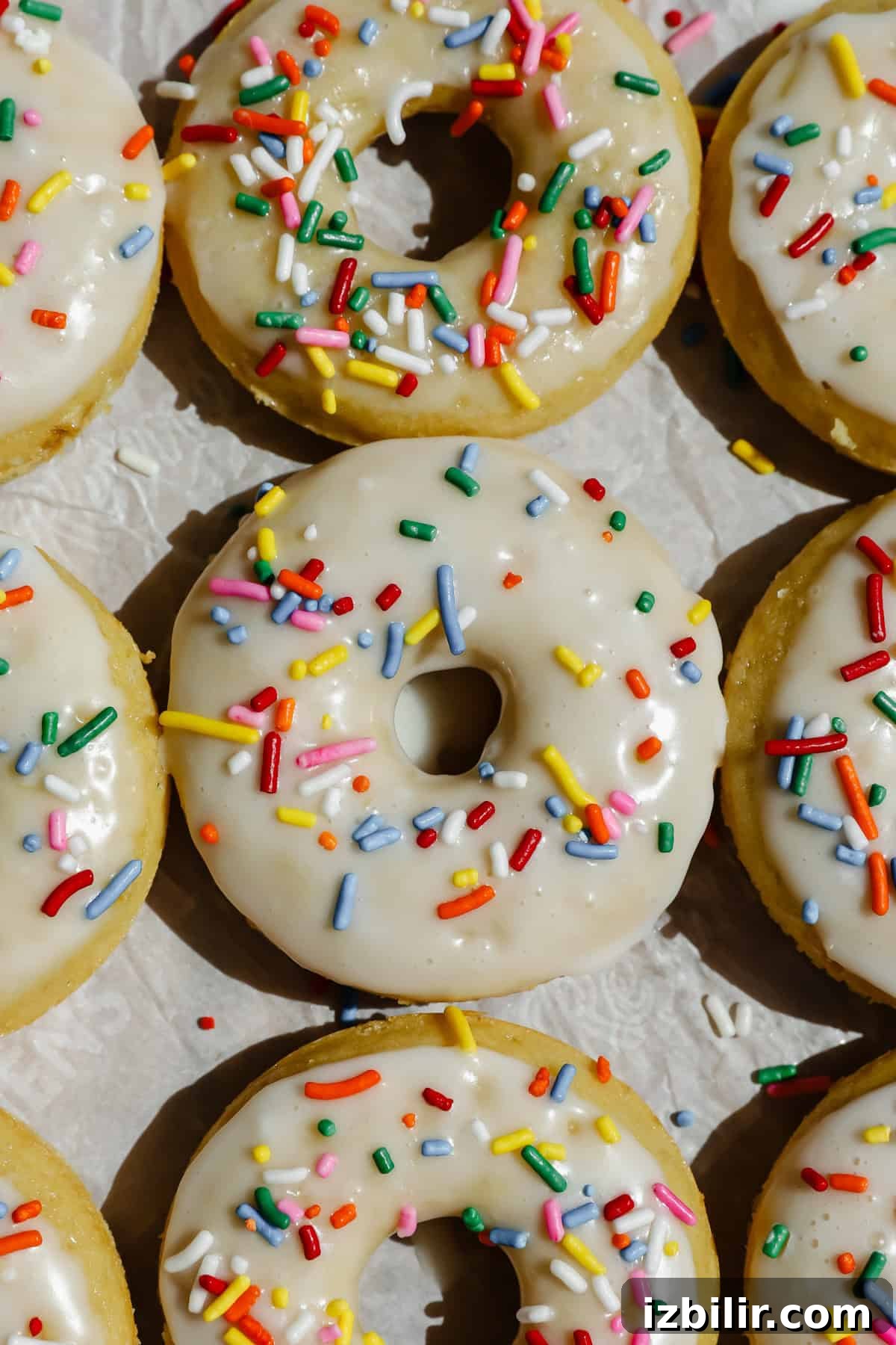 Glazed donuts topped with colorful sprinkles are arranged closely together on a light surface.