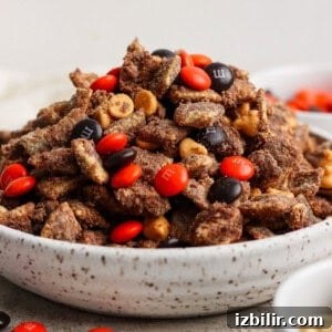 No-Bake Pumpkin Spice Protein Puppy Chow Recipe 5 A bowl filled with chocolate-coated nuts or snack mix, topped with orange and brown M&M’s and butterscotch chips.