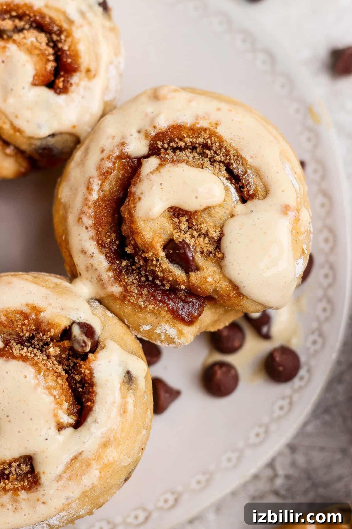 High-Protein Cottage Cheese Recipes for Fall 4 Close-up of cinnamon rolls topped with icing on a decorative white plate, with several chocolate chips scattered nearby.