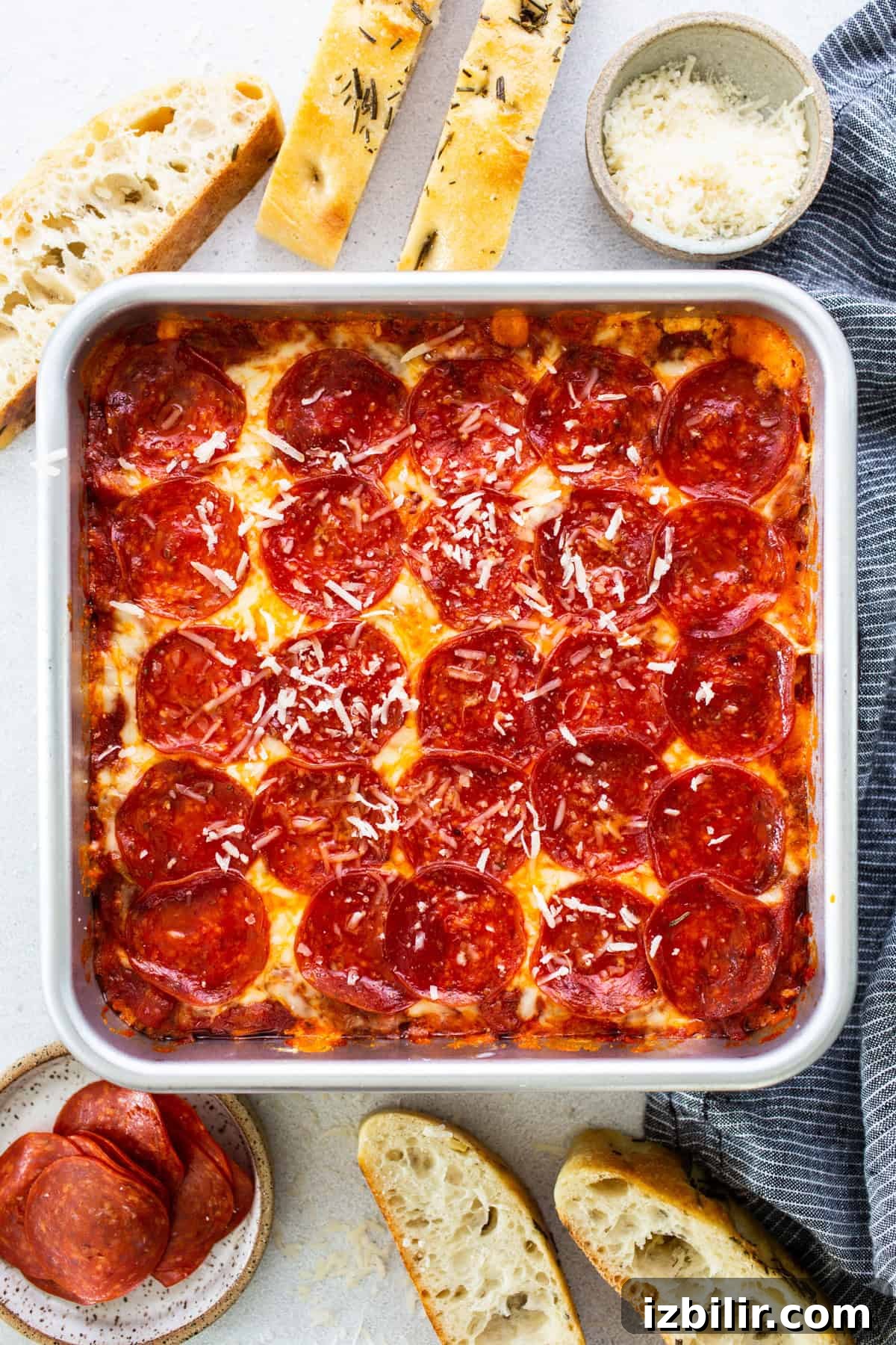 High-Protein Cottage Cheese Recipes for Fall 6 Square deep-dish pepperoni pizza in a pan, surrounded by bread slices, grated cheese in a bowl, and a small plate of pepperoni slices on a light surface.