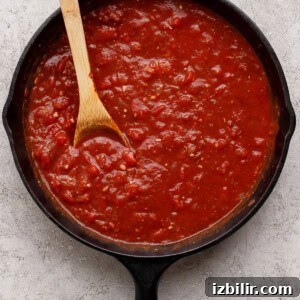 A cast iron skillet filled with chunky tomato sauce, with a wooden spoon resting inside.