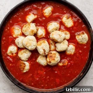 A cast iron skillet filled with meatballs in tomato sauce on a light textured surface.