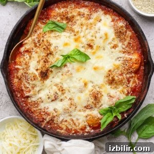 A cast iron skillet filled with baked cheesy tomato dish, garnished with fresh basil.