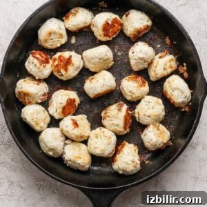 Cooked meatballs are arranged in a black cast iron skillet on a light textured surface.