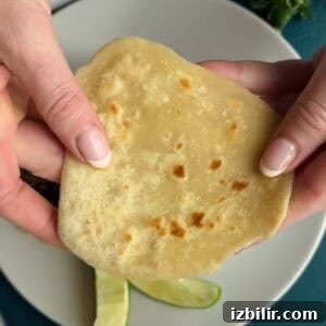 Two hands hold a flatbread over a plate containing lime wedges.