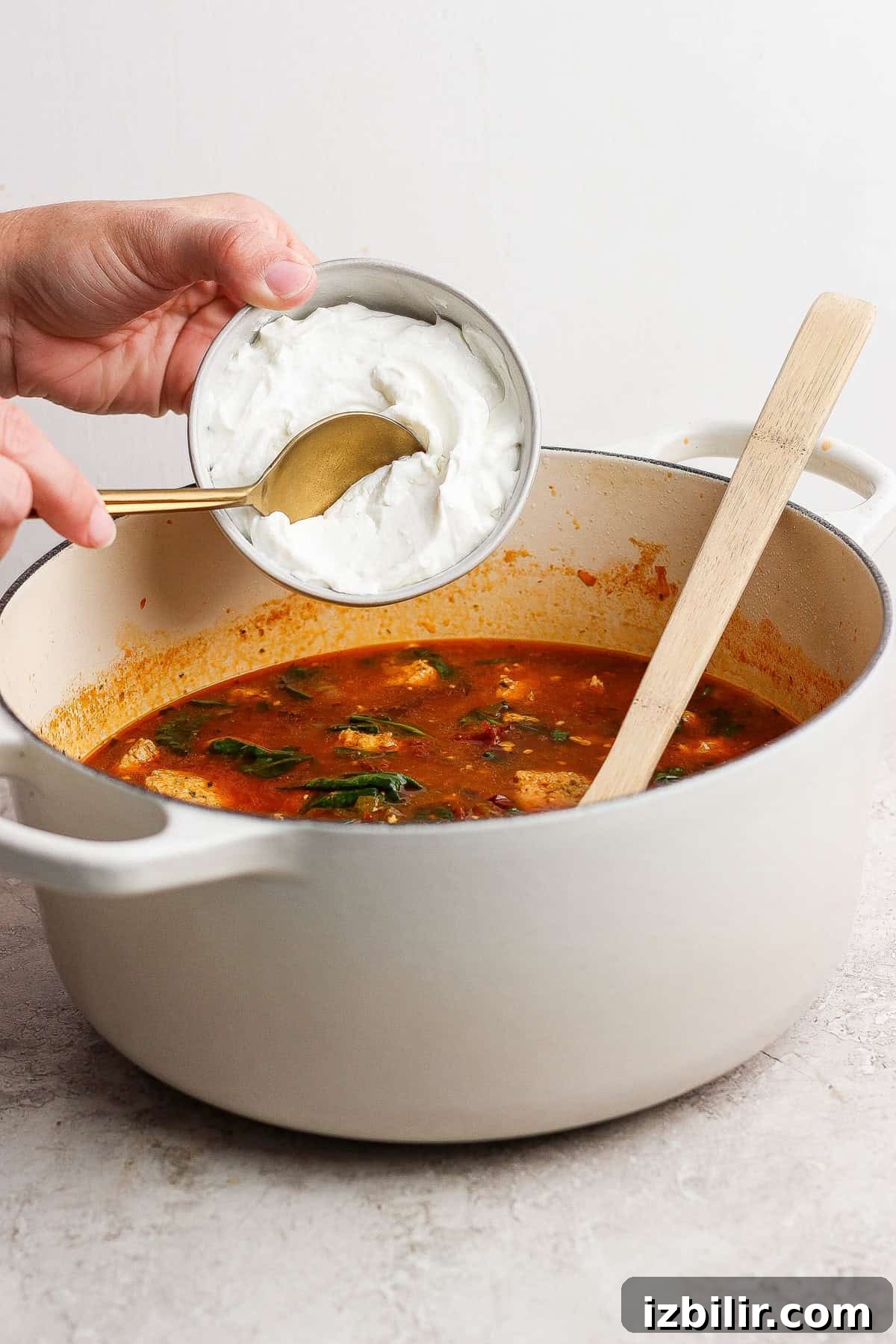 A person pouring cream into a pot of soup.