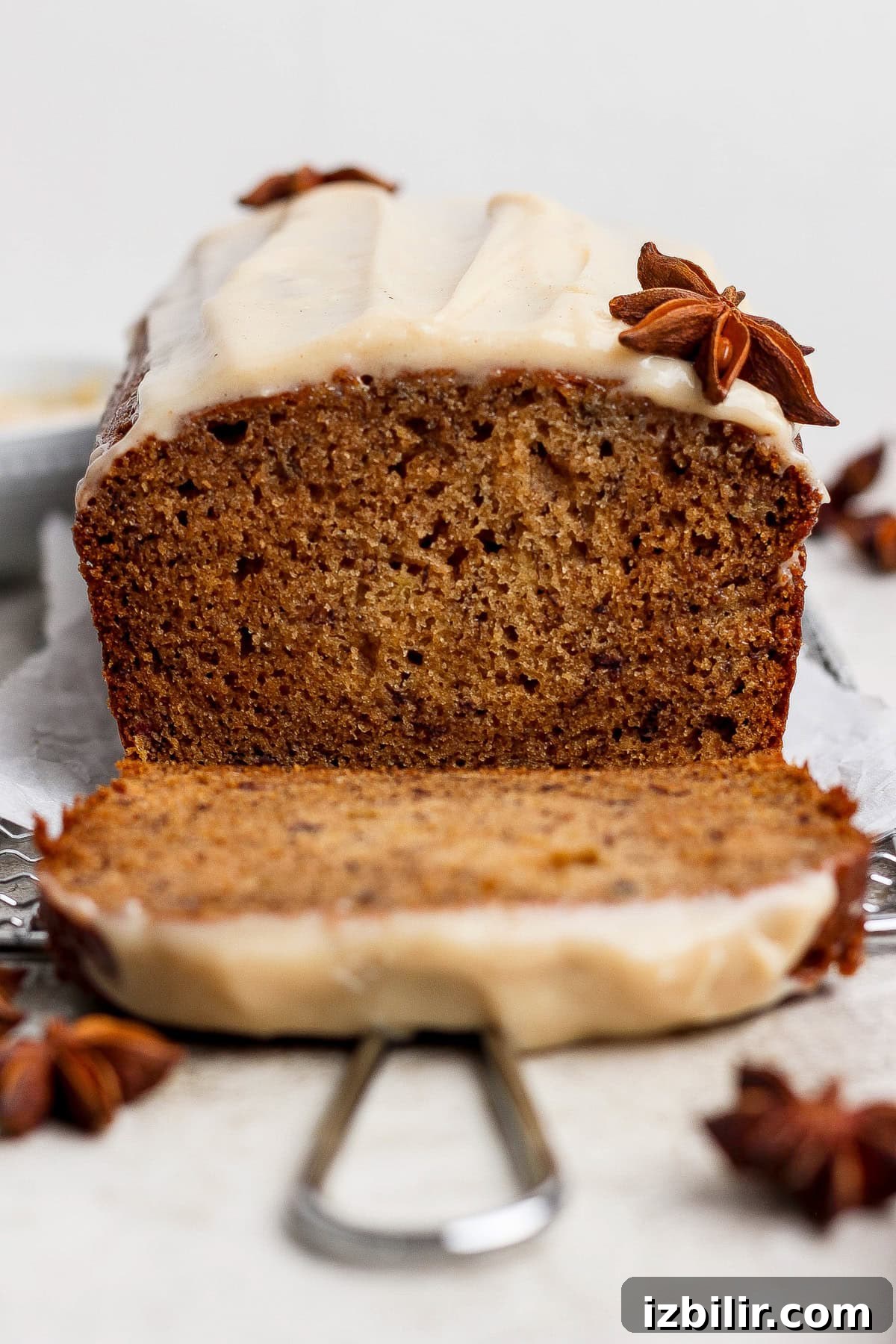 A loaf of spiced banana bread is sliced, topped with a light frosting and star anise decorations placed on and around the bread—a delicious twist on a classic banana bread recipe.