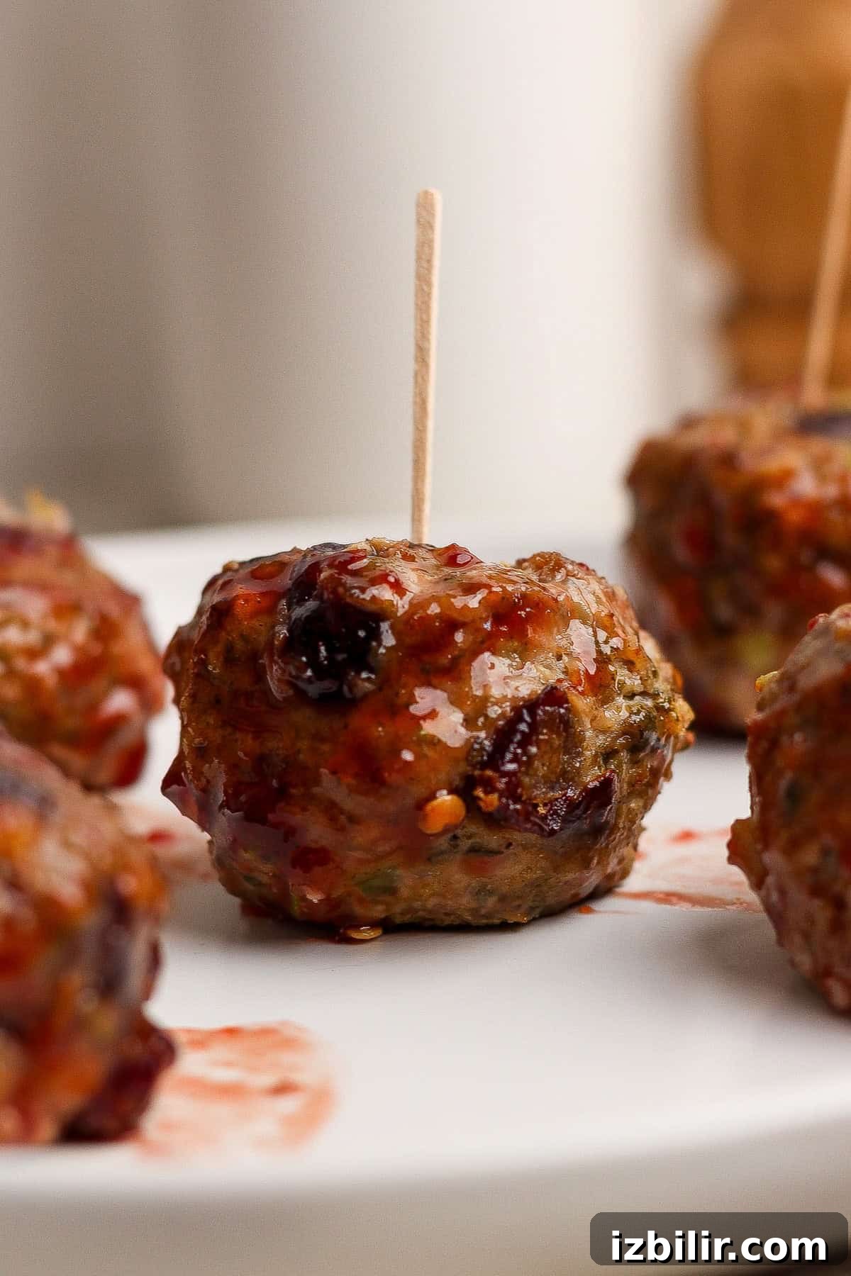 Thanksgiving Meatballs Recipe with Raspberry Sauce 2 A close-up of glazed meatballs on a white plate, each with a toothpick inserted for serving.