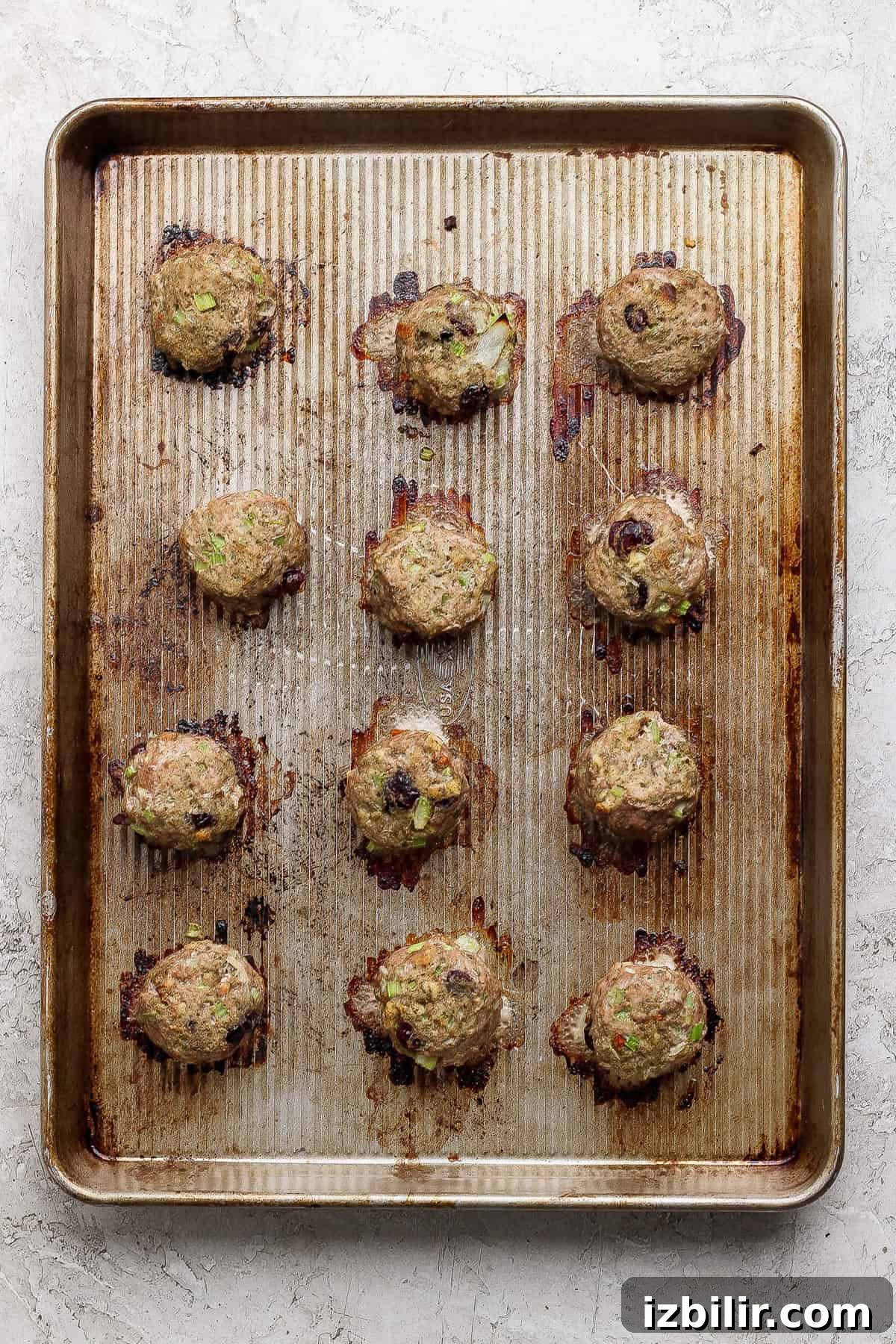 Thanksgiving Meatballs Recipe with Raspberry Sauce 5 A baking sheet with twelve cooked meatballs, spaced apart, on a ridged metal tray with visible browning and juices.