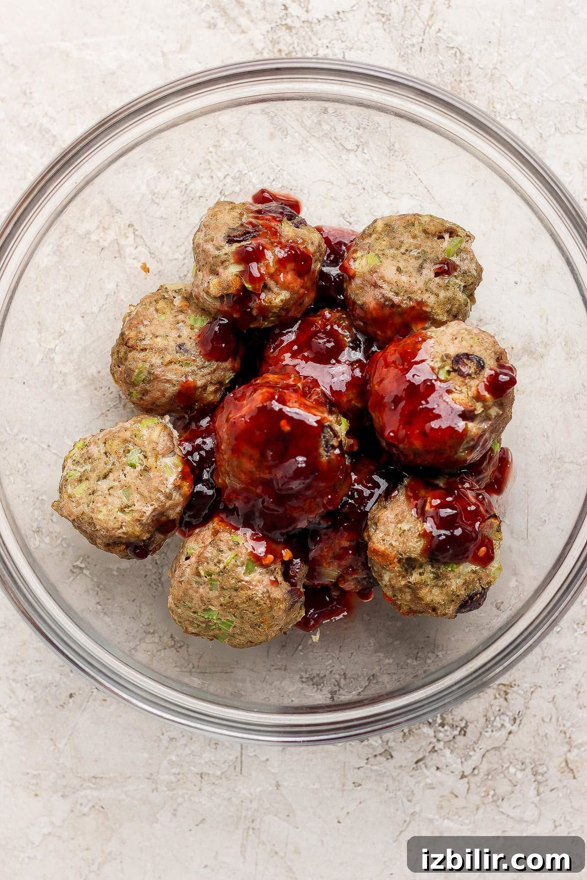 Thanksgiving Meatballs Recipe with Raspberry Sauce 6 Meatballs coated with a dark sauce arranged in a glass bowl on a light textured surface.