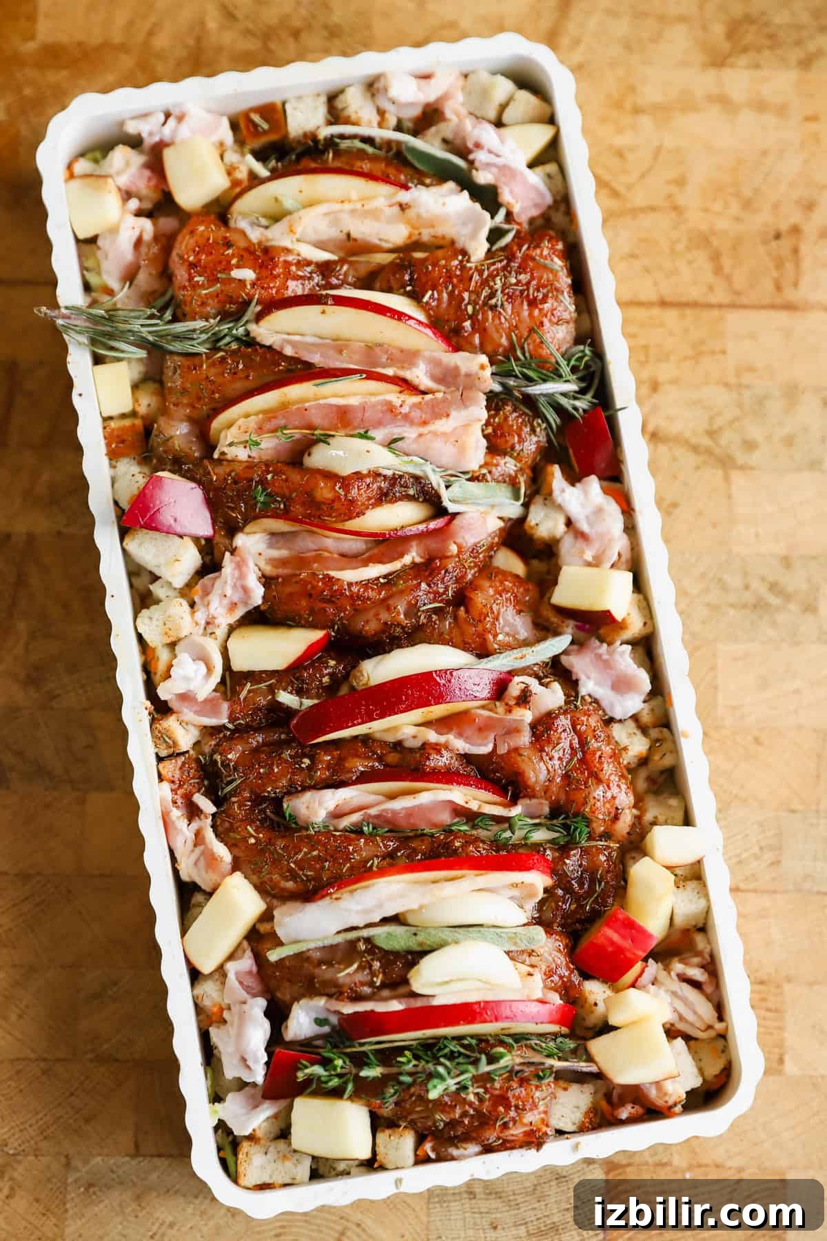 Sheet-Pan Thanksgiving Dinner for 4: Complete One-Tray Menu 3 Raw seasoned turkey tenderloin topped with apple slices and herbs, arranged in a rectangular baking dish with cubed bread and chopped apples.