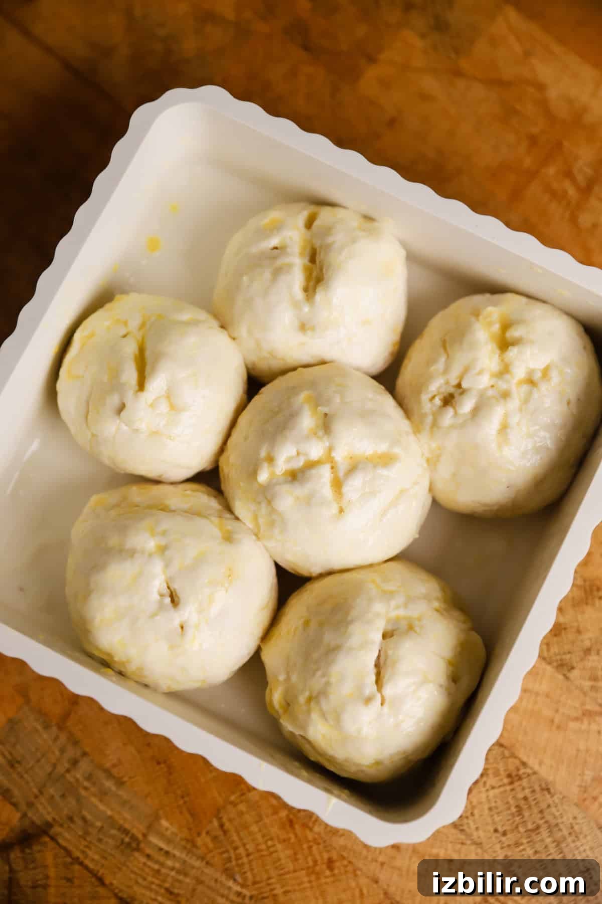 Sheet-Pan Thanksgiving Dinner for 4: Complete One-Tray Menu 5 Six unbaked dough balls evenly arranged in a white baking dish, placed on a wooden surface.