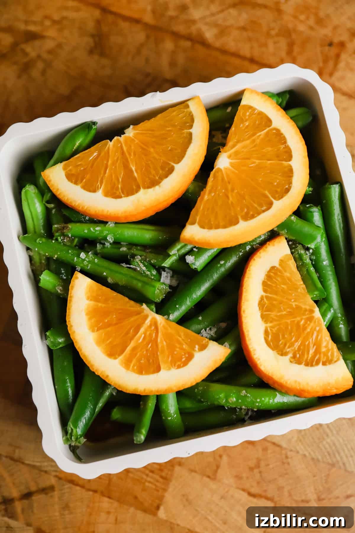 Sheet-Pan Thanksgiving Dinner for 4: Complete One-Tray Menu 6 A white dish filled with green beans, topped with four orange slices, set on a wooden surface.