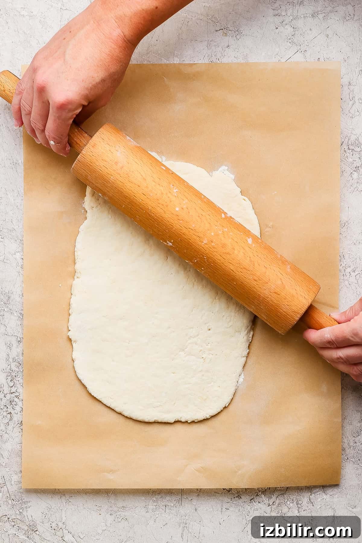 Protein-Packed Garlic Parmesan Cottage Cheese Dinner Rolls 3 A person uses a wooden rolling pin to flatten dough on a sheet of parchment paper placed on a textured surface.