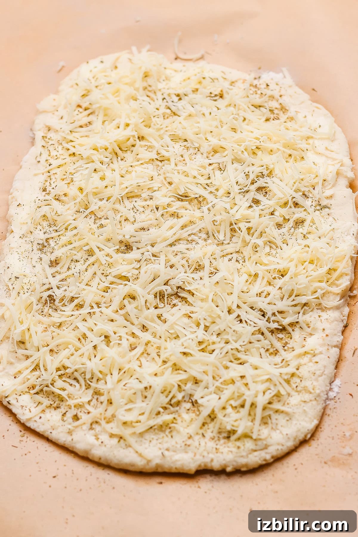 Protein-Packed Garlic Parmesan Cottage Cheese Dinner Rolls 4 Unbaked flatbread dough topped with shredded cheese and herbs on a sheet of parchment paper.